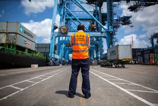 A port officer in a high-visibility vest watching ship-to-shore cranes at the Port of Mombasa
